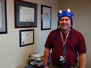 man wearing a hat standing next to diplomas on a wall