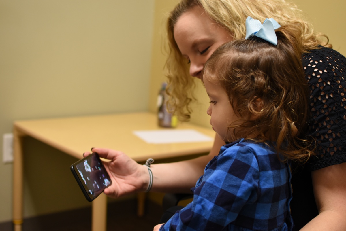 woman holding baby in lap, watching phone