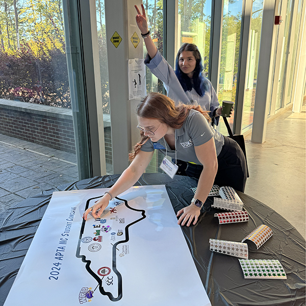 a student placing a Duke sticker on a map of NC