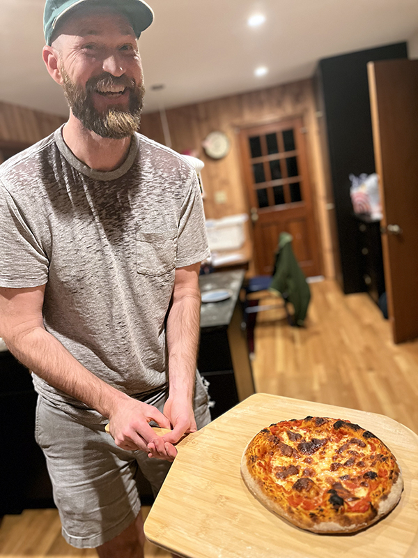 marcus holding a pizza server with a pizza on it