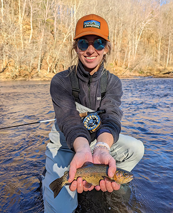 Grace Futch holding a fish she caught while kneeling in a stream. 