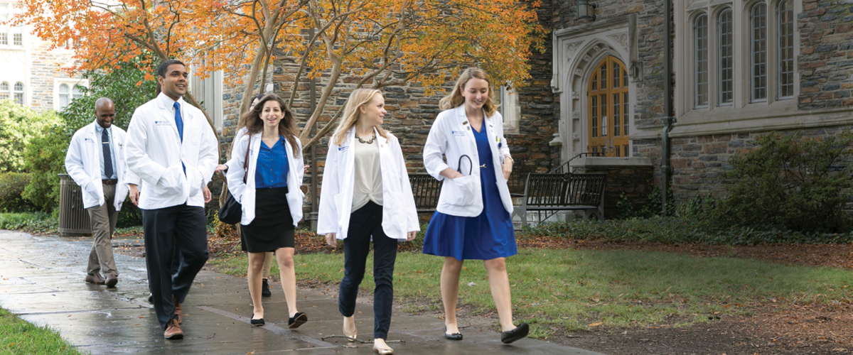 MD Students in white coats walking on the West Campus Quad with fall foliage in the background